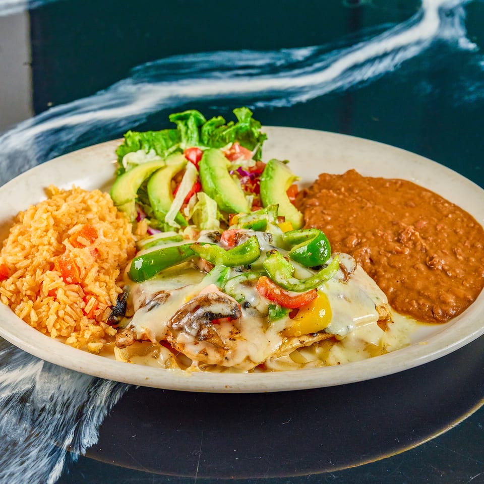Mexican-style platter with cheesy grilled chicken, peppers, avocado salad, Spanish rice, and refried beans.