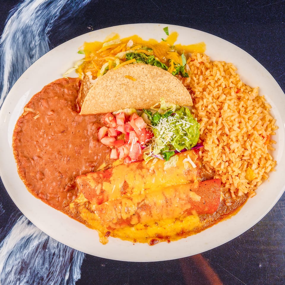 Mexican combination plate with a crispy taco, cheese-covered enchiladas, refried beans, Spanish rice, guacamole, lettuce, and tomatoes.