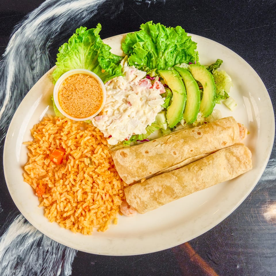 Plate of Mexican-style rice, burritos, creamy salad, avocado slices, lettuce, and dipping sauce.