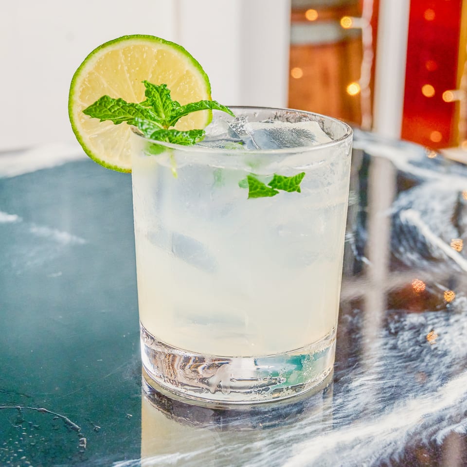 Iced lime and mint cocktail in a clear glass on a reflective table, garnished with a lime wheel and fresh mint.