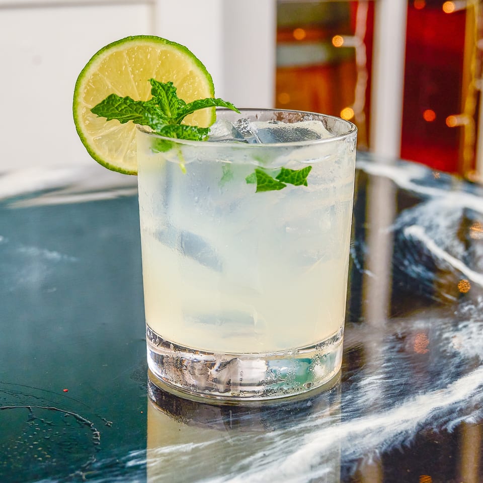 Chilled lime and mint cocktail with ice in a tumbler, garnished with a lime wheel, on a reflective bar.