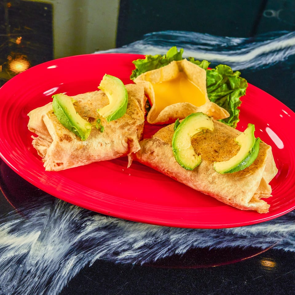 Grilled burritos topped with avocado slices, served with lettuce and tortilla chips on a bright red plate.