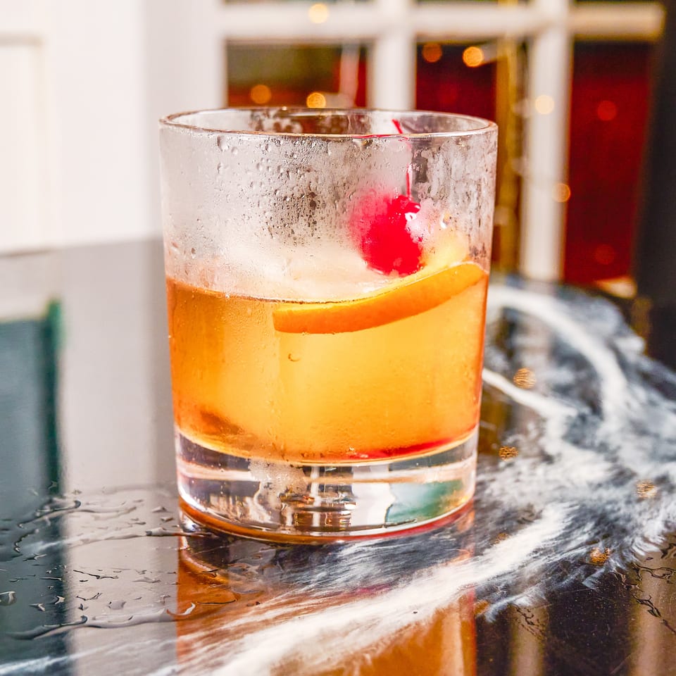 Citrus cocktail with an orange slice and red cherry garnish in a chilled glass on a reflective bar.