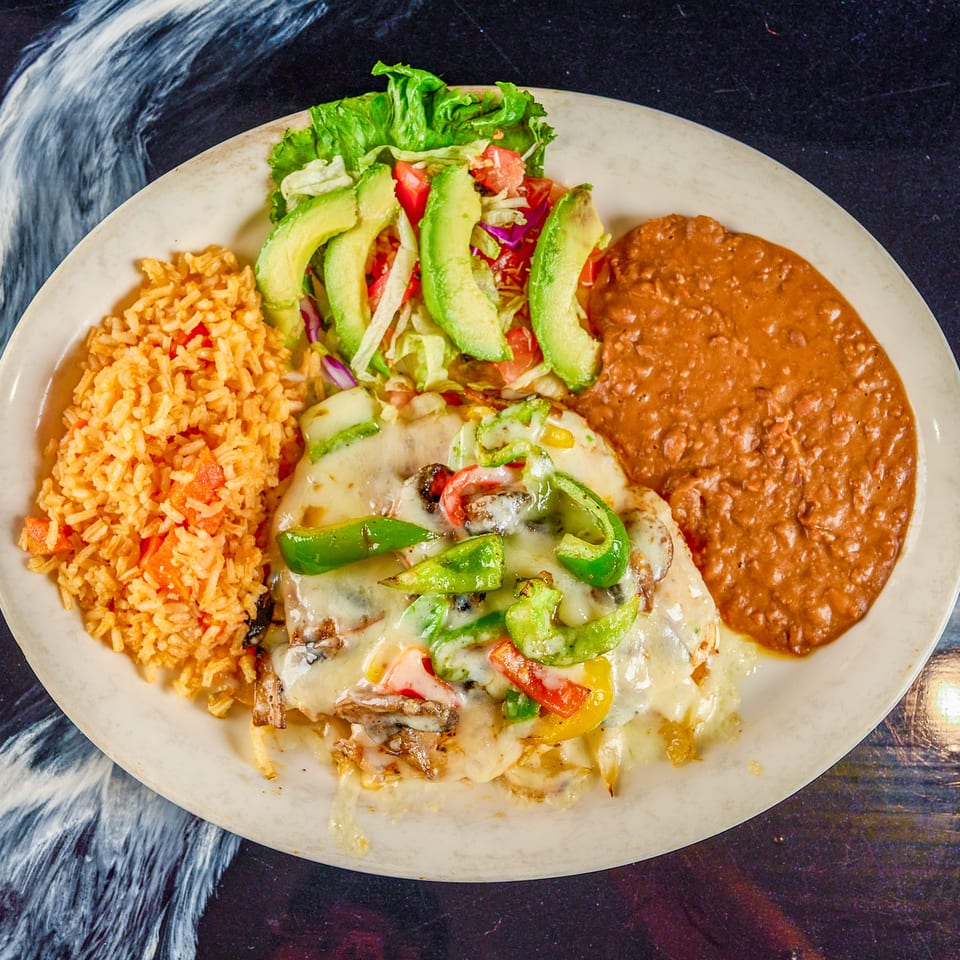 Mexican-style plate with cheesy grilled meat, peppers, avocado salad, Spanish rice, and refried beans.